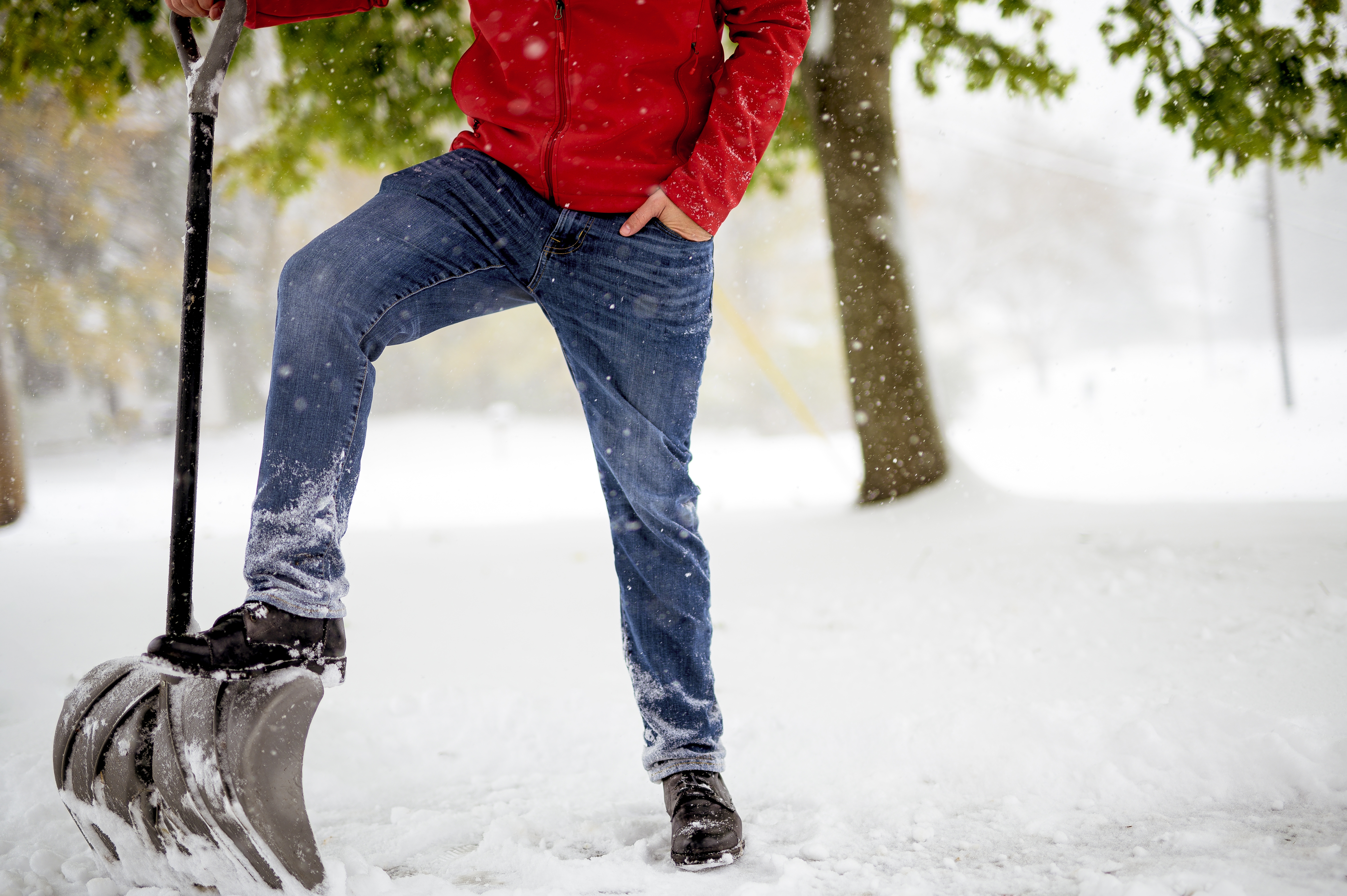 A closeup shot fo a male with his foot on the snow shovel while standing in a snowy field